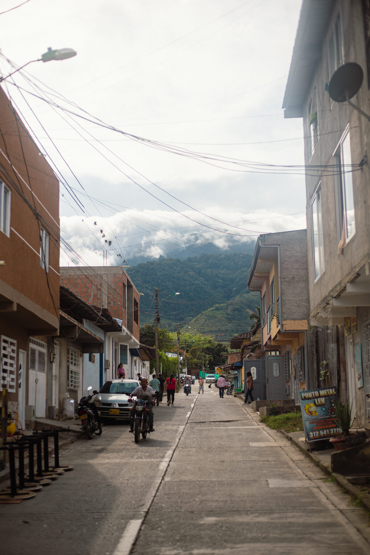 A street in Calima El Darien running down towards cloud-covered green mountains, with motorbikes and people going about their day