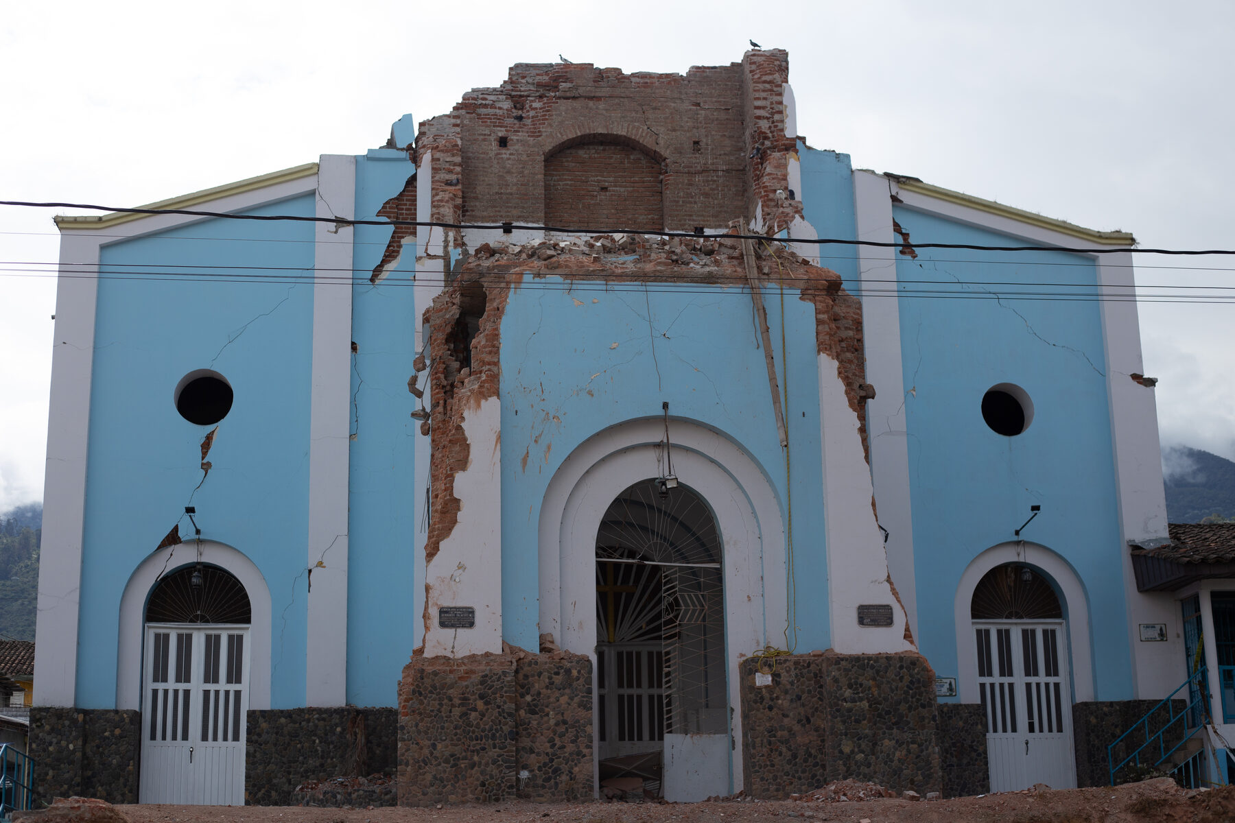 The blue town church with its brick bell tower collapsed and a deep crack running down the facade
